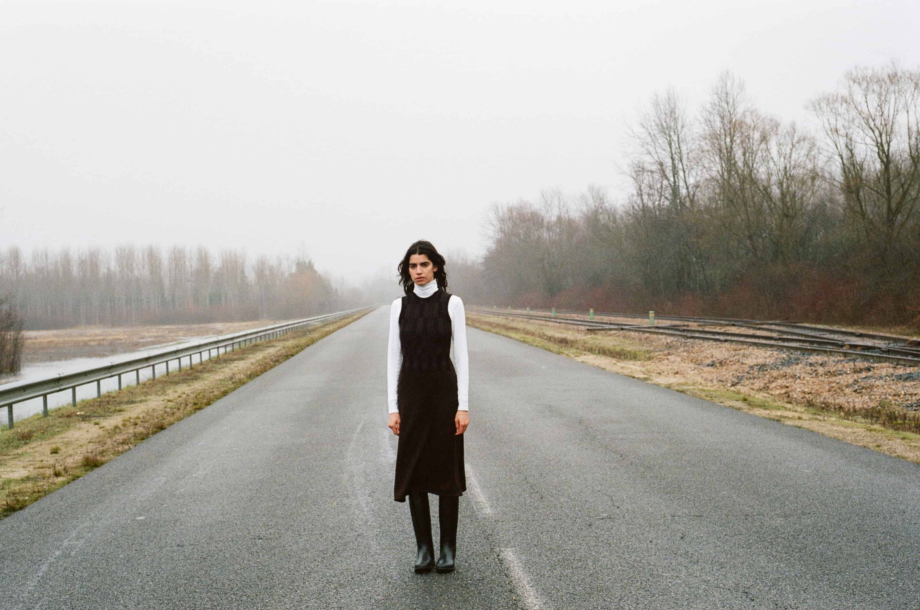 Model wearing black & brown grid vest over white turtleneck top and brown knitted skirt