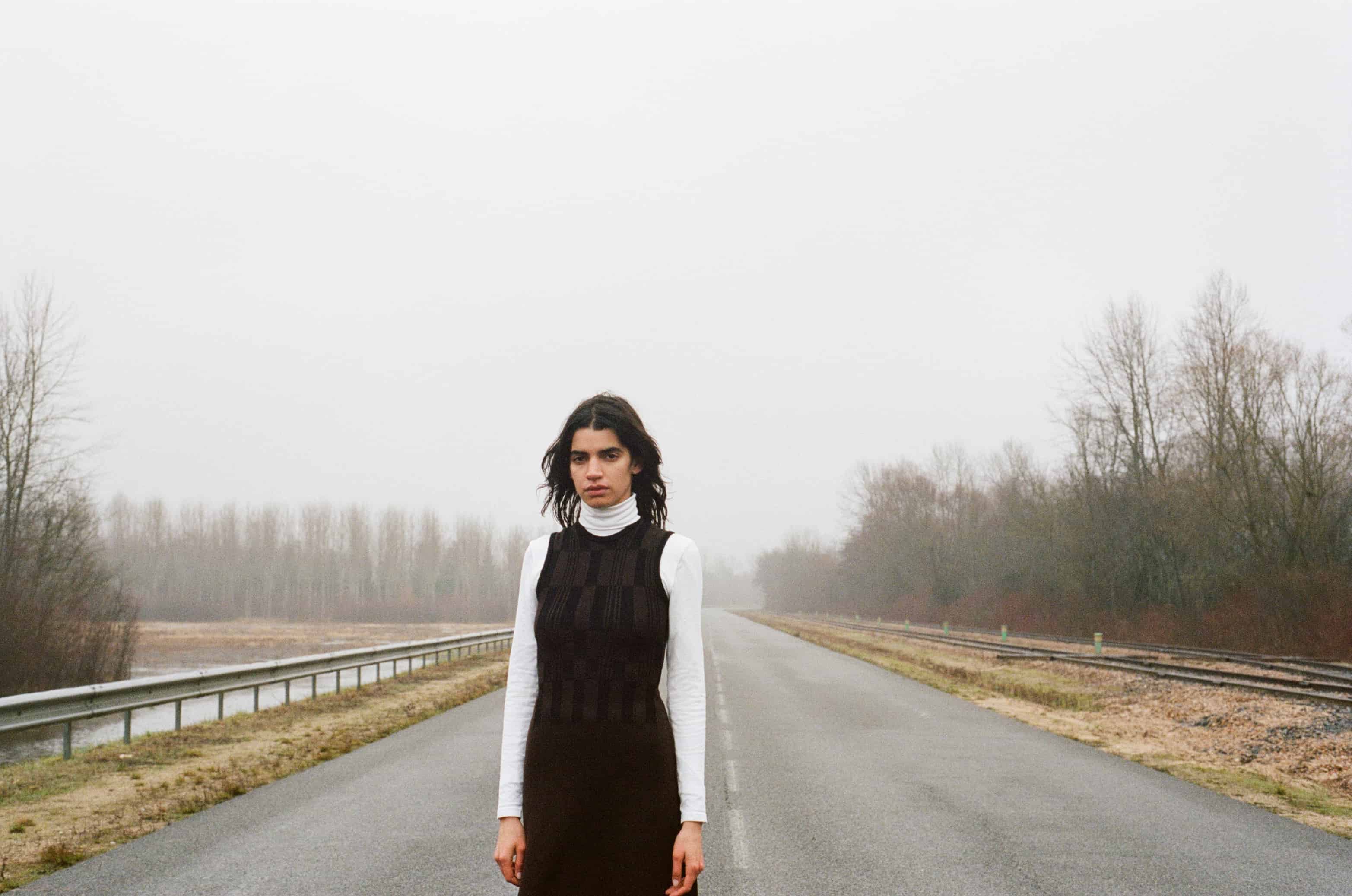 Model wearing black & brown grid vest over white turtleneck top and brown knitted skirt