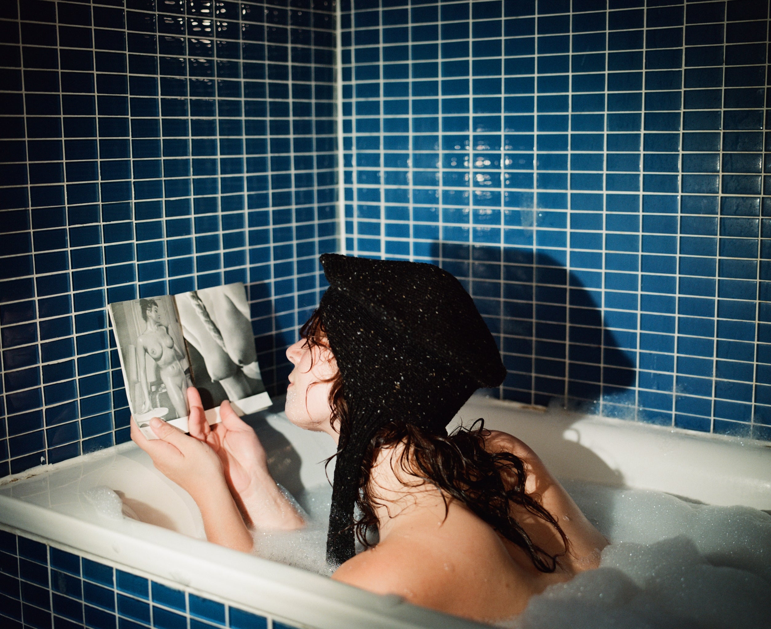 Model reading a book in a bubble bath wearing the classic hat in Donegal Tweed in black