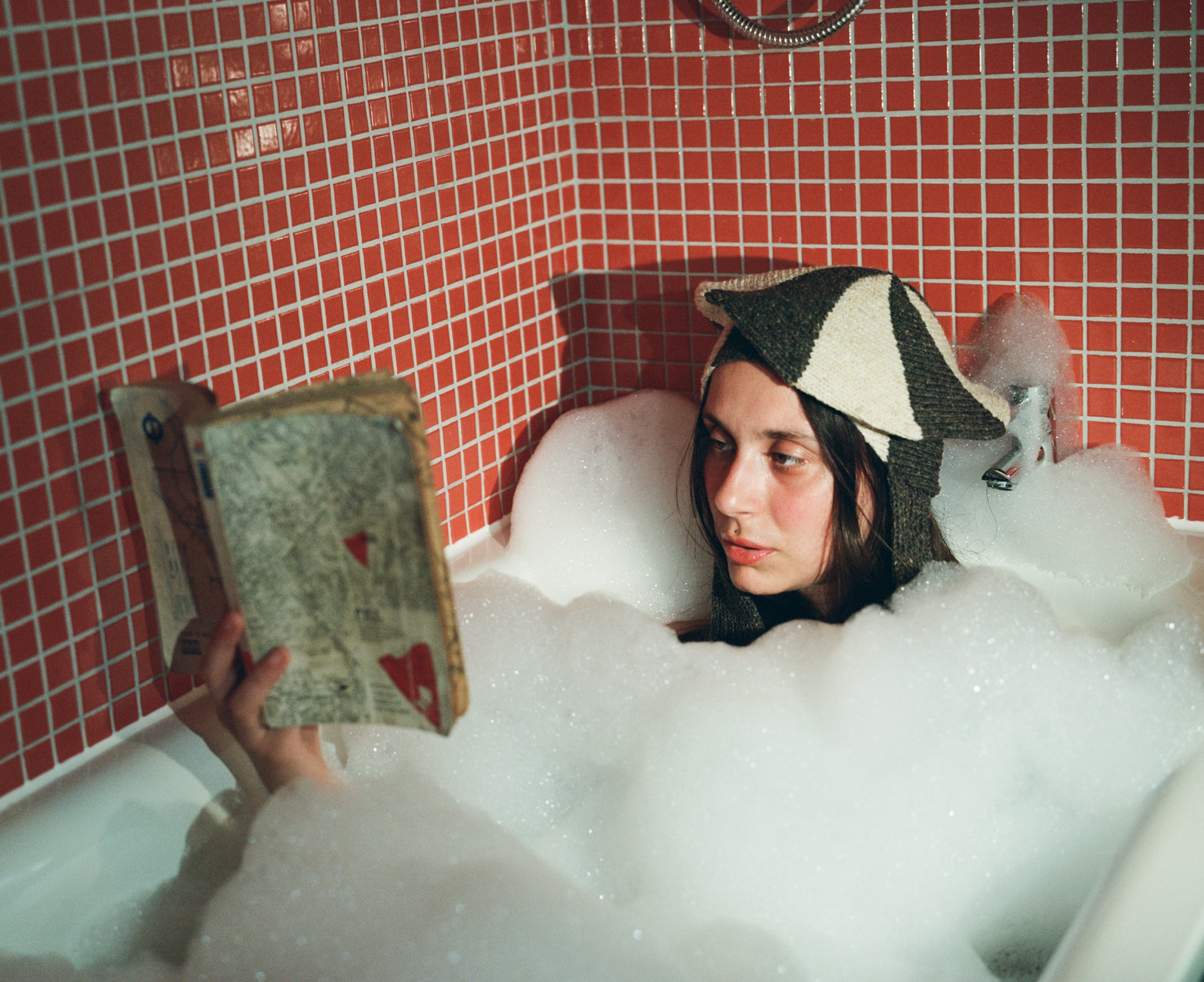 Model reading a book in a bubble bath wearing the spiral classic hat in donegal tweed in grey & beige