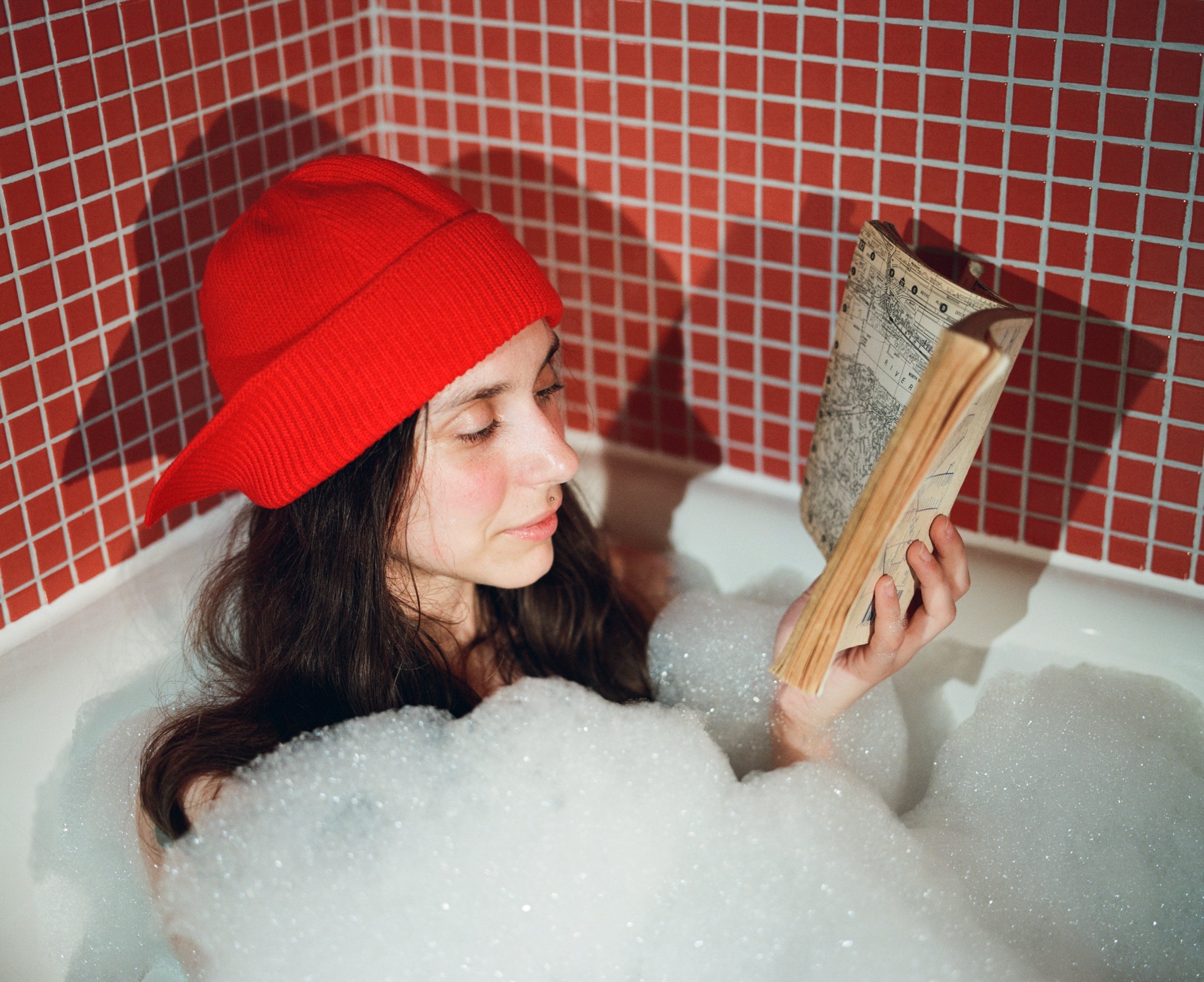 Model reading a book in a bubble bath wearing the Flap hat in red