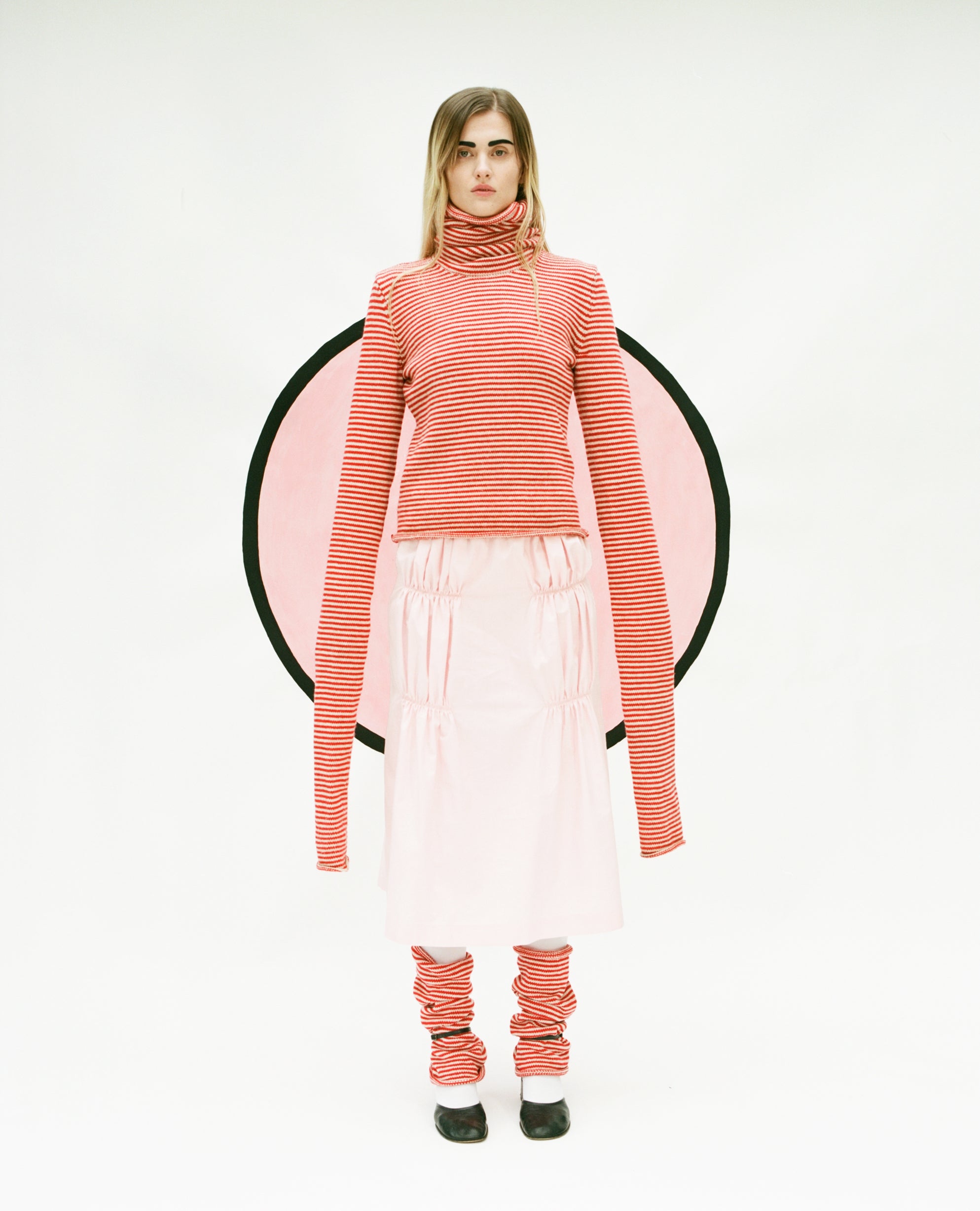 Model wearing stripy Double Snood top in red & oatmeal, Ruche cotton skirt in pink and stripy snood leg warmers also in red & oatmeal