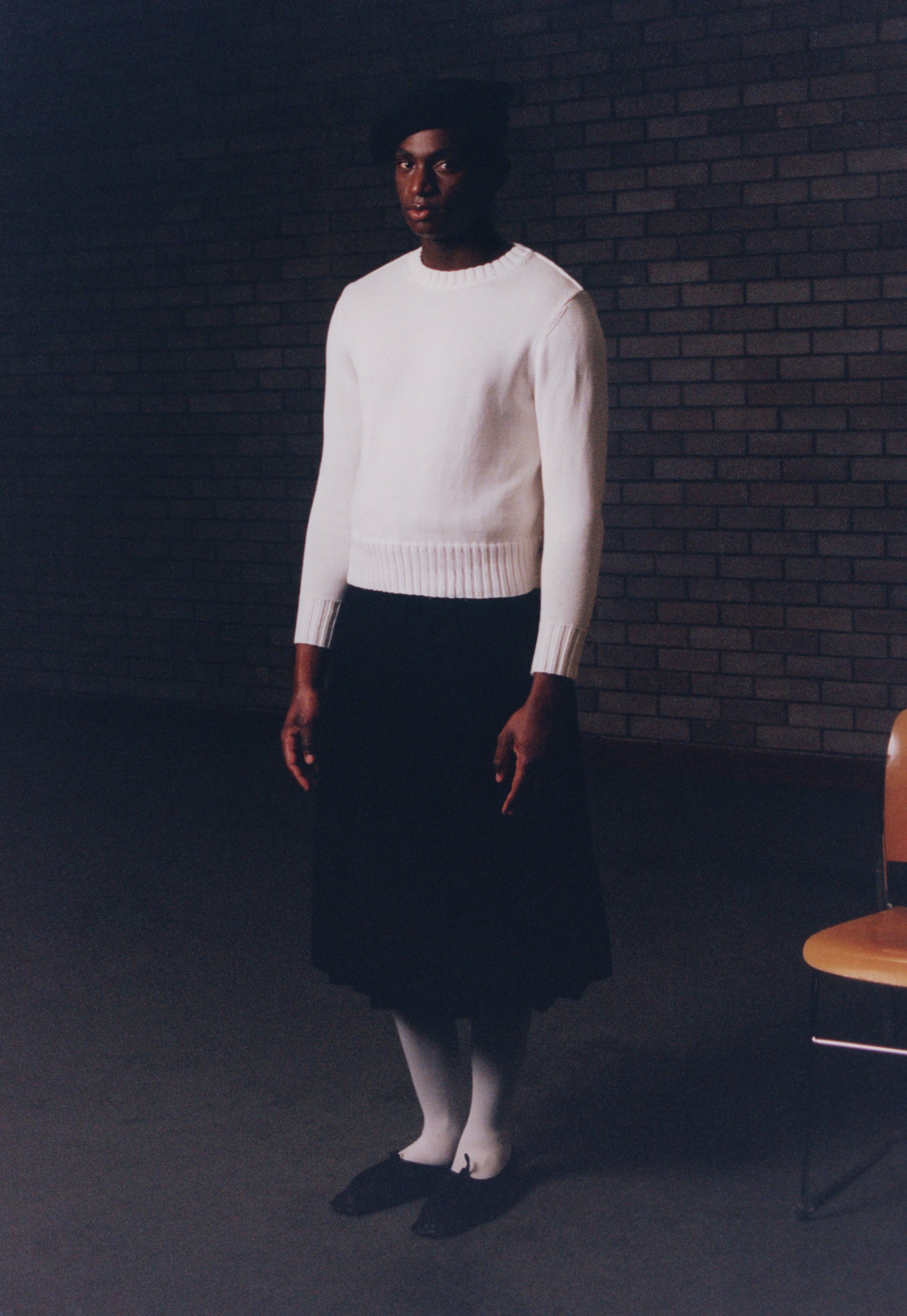 Look 4 - model wearing sack hat in black, traditional sweater in ecru, black wool skirt and black flat lace-up shoes