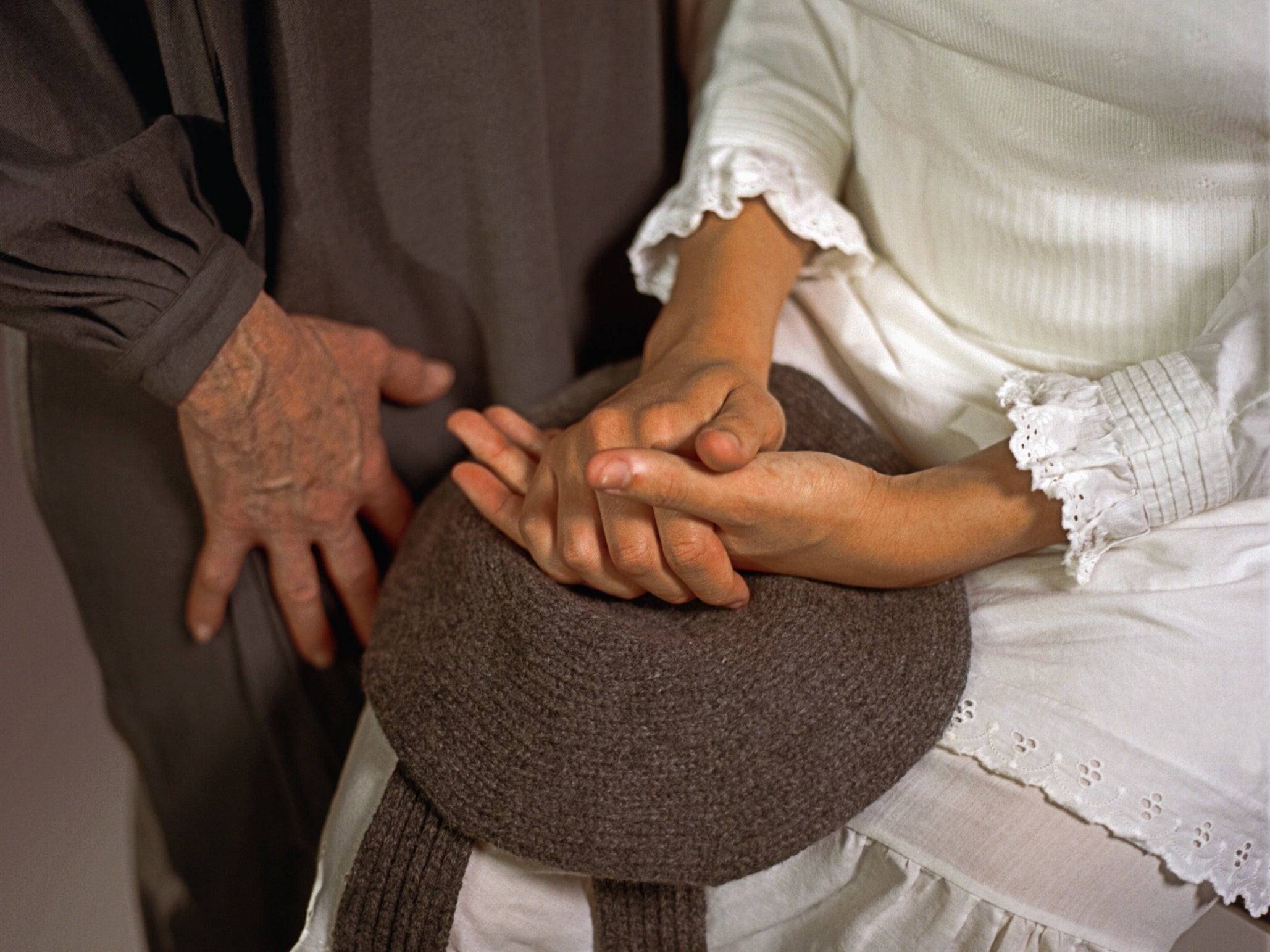 Close up of model's hands resting on top of classic hat in chocolate brown