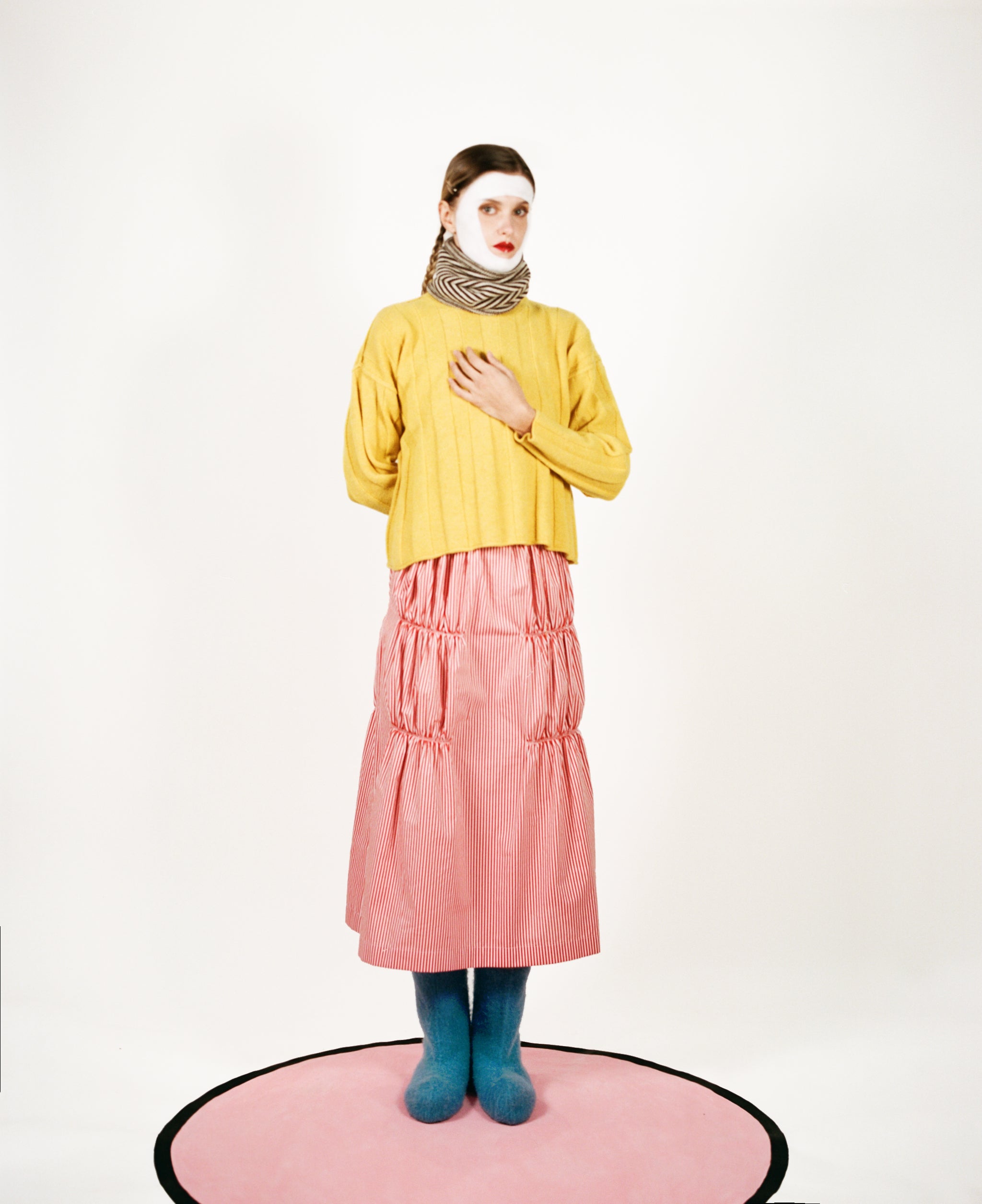 Model wearing stripy snood, wide-rib sweater in yellow, ruche cotton skirt in red & oatmeal and blue felt boots